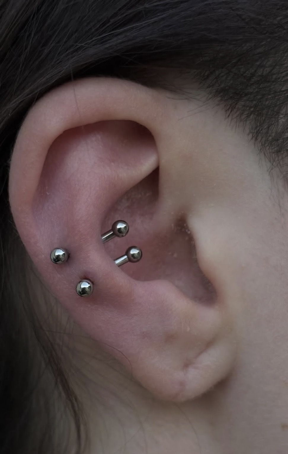 Oreille avec plusieurs piercings argentés et boucle pendante